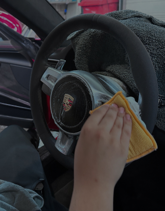 Stuur van een Porsche wordt gereinigd met een microvezeldoek tijdens interieurbehandeling