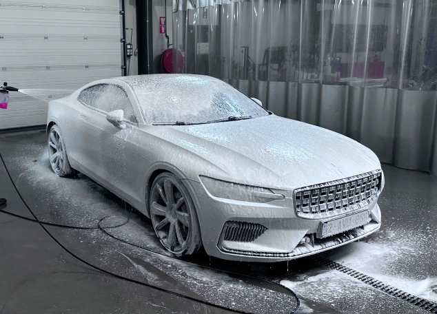 Witte sportcoupé bedekt met actief snow foam tijdens de pre-wash fase van car detailing